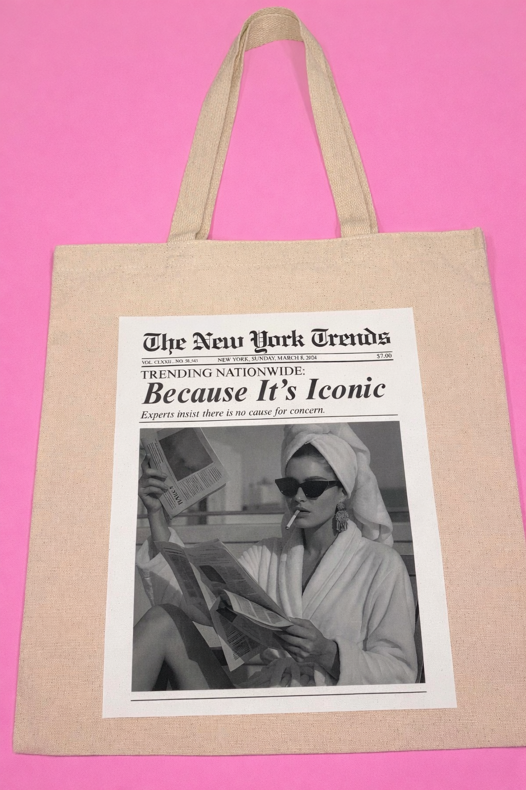 Beige tote bag with a printed newspaper design of a woman in sunglasses and a towel with title "Because It's Iconic"