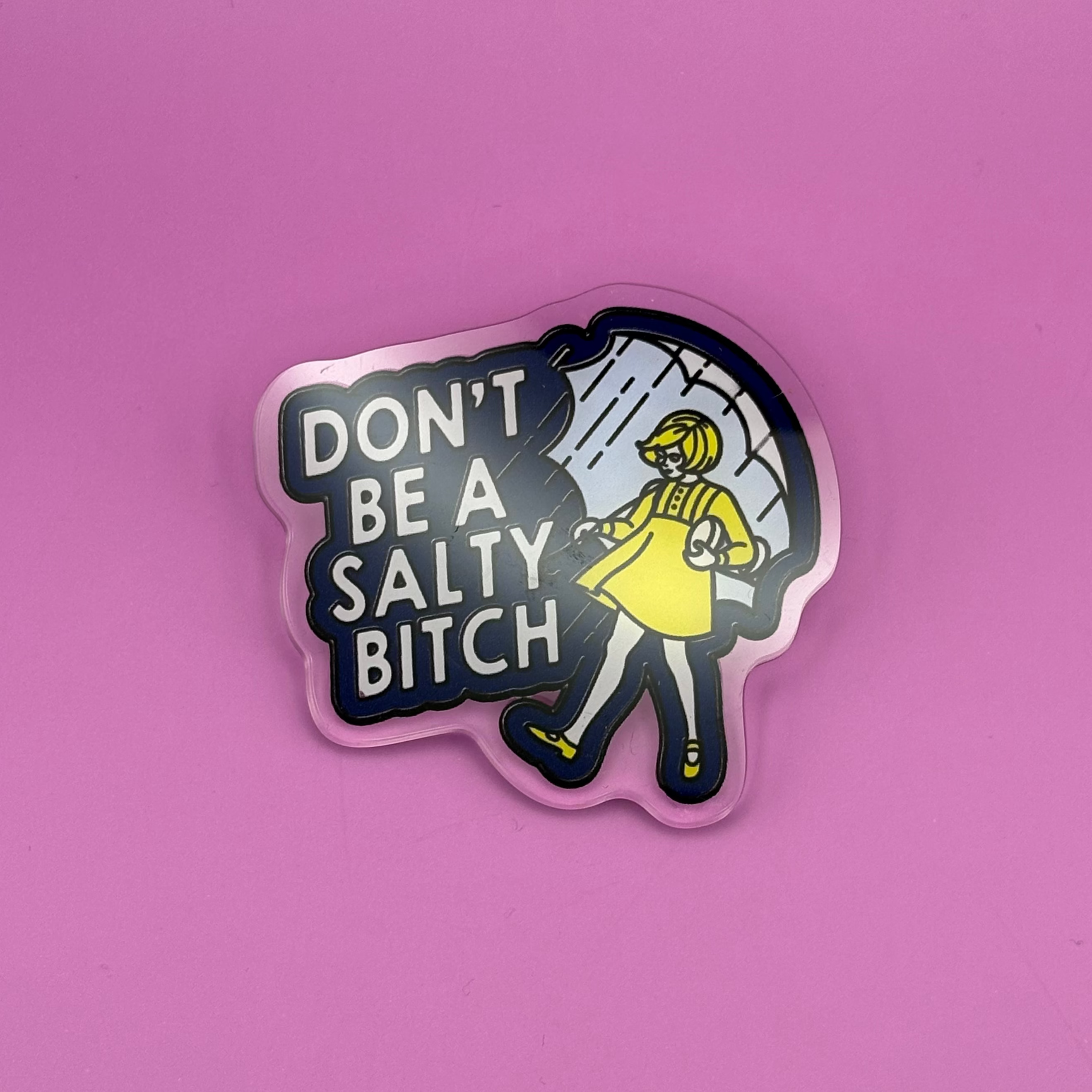 A die-cut sticker featuring a cartoon illustration of a person in a yellow raincoat and black pants with the text 'DON'T BE A SALTY BITCH' in white, shown on a solid pink background.