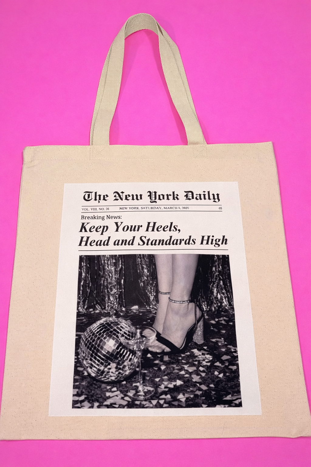 Tote bag with a newspaper design featuring a headline "Keep Your Heels, Head, and Standards High" and image of a woman in high heels and next to a small disco ball.