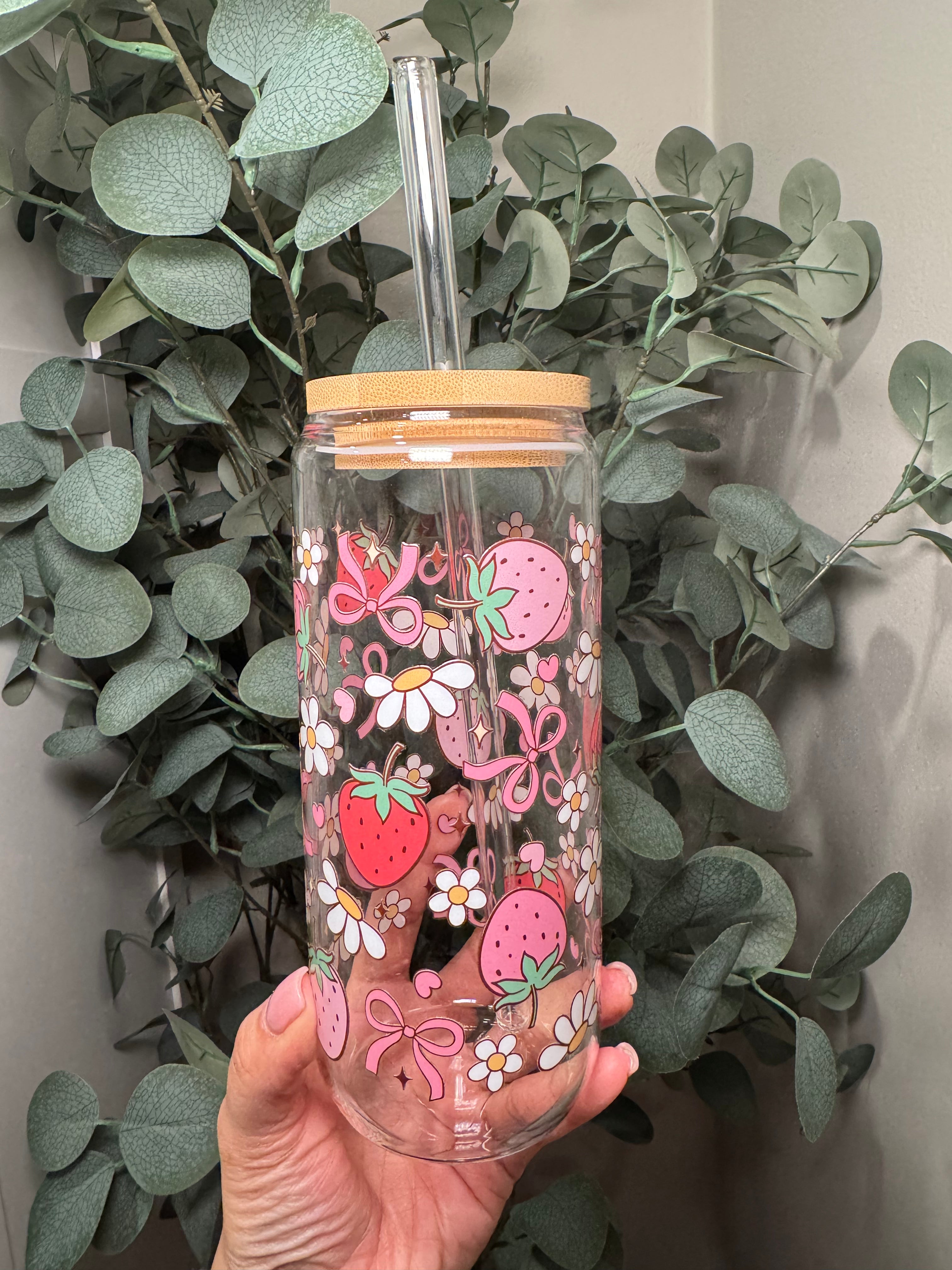 Glass cup with straw and lid and strawberry, flower and bow design in pink, green and white