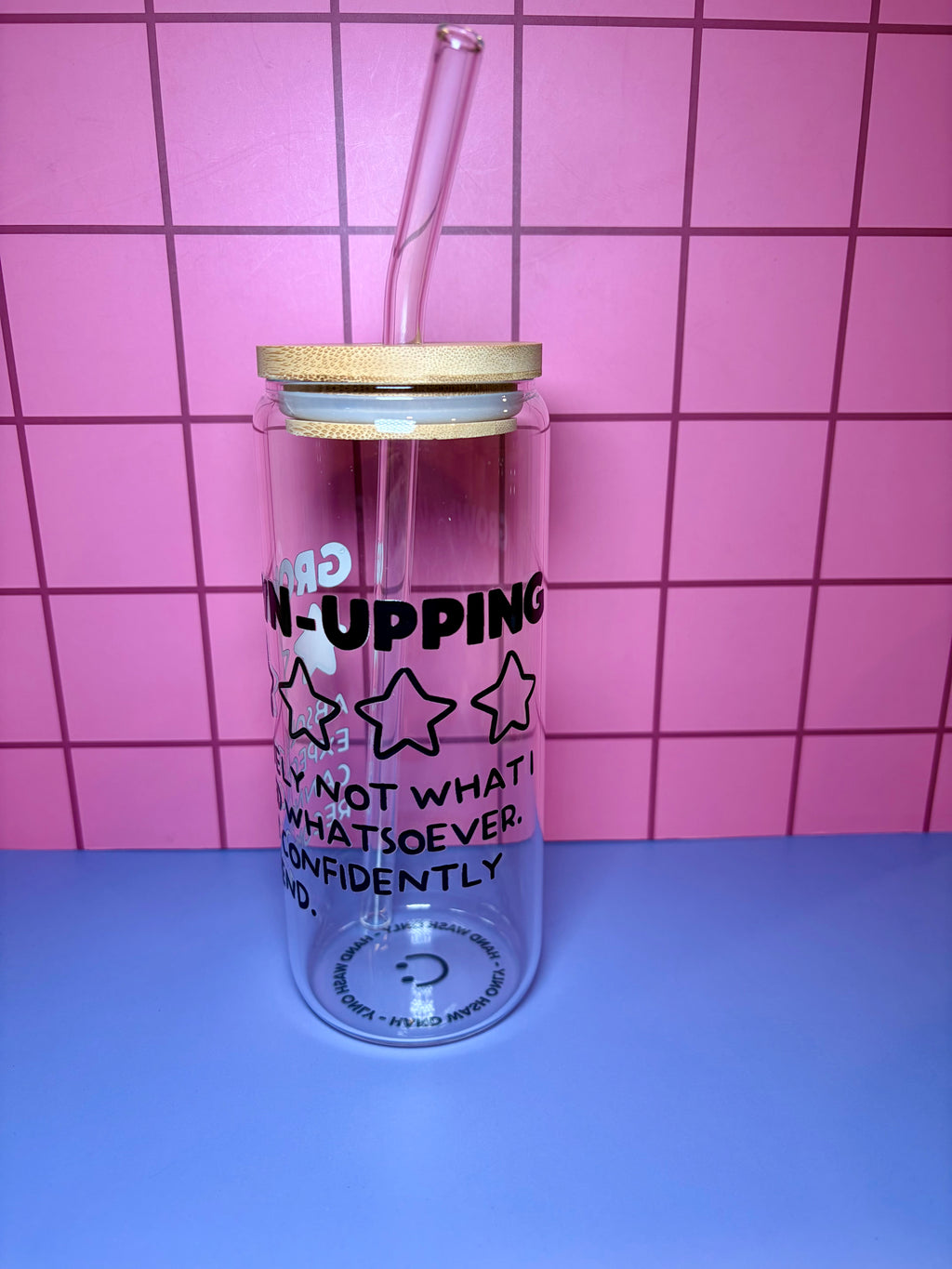 Clear tumbler with straw and text against a pink tiled wall