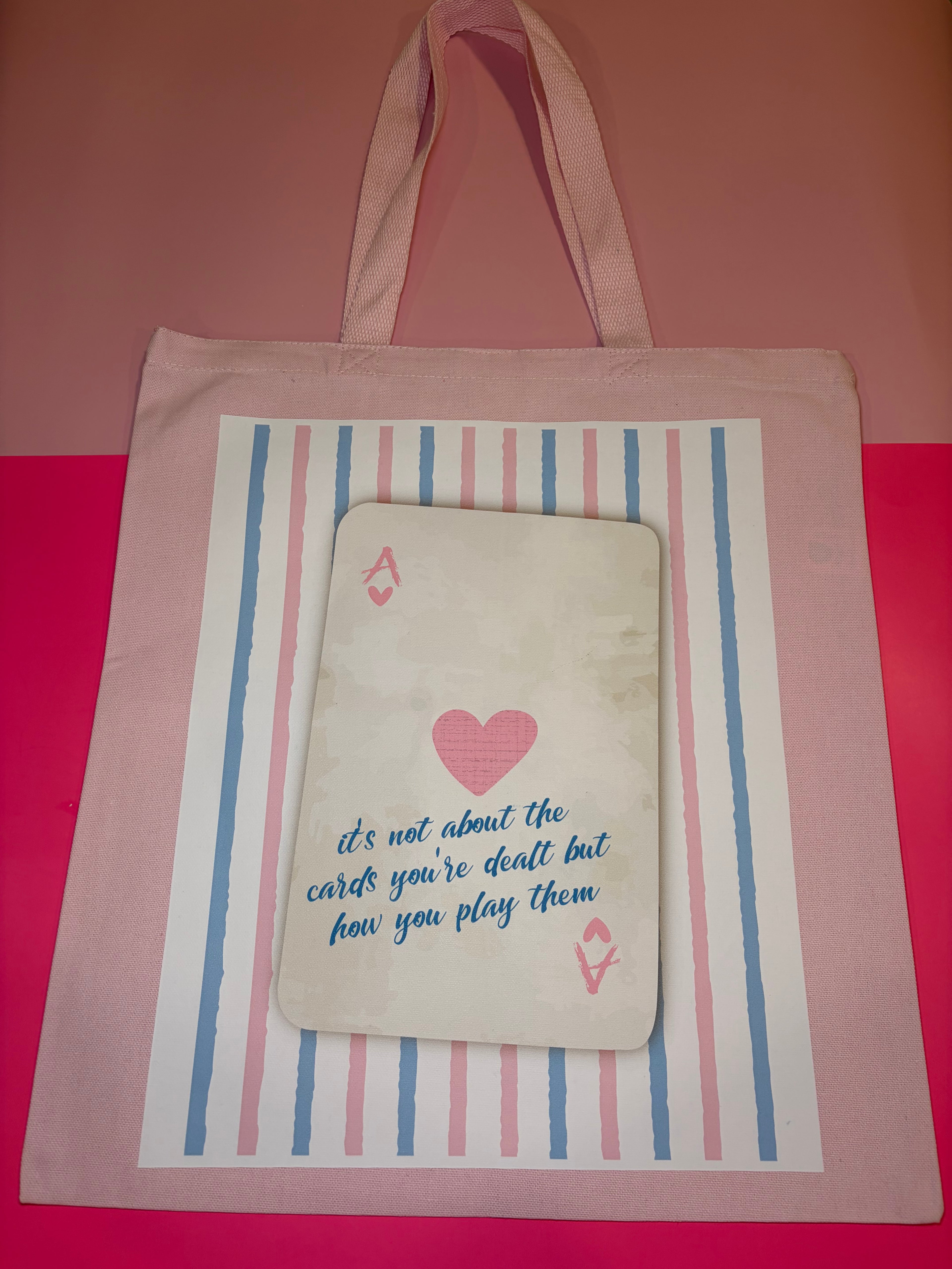 Pink tote bag with playing card design and text on a pink and red background