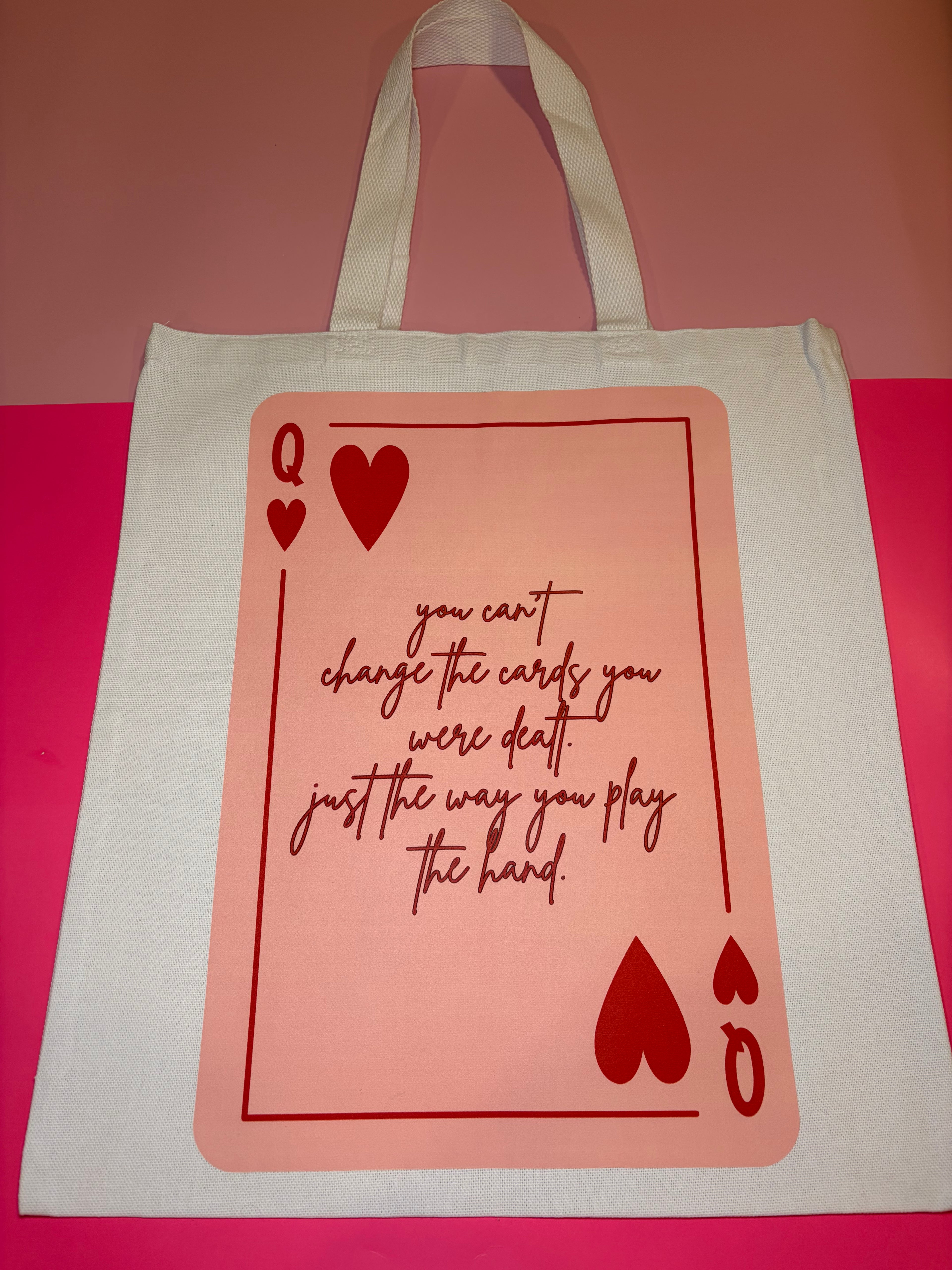 Tote bag with playing card design and red text on a pink background