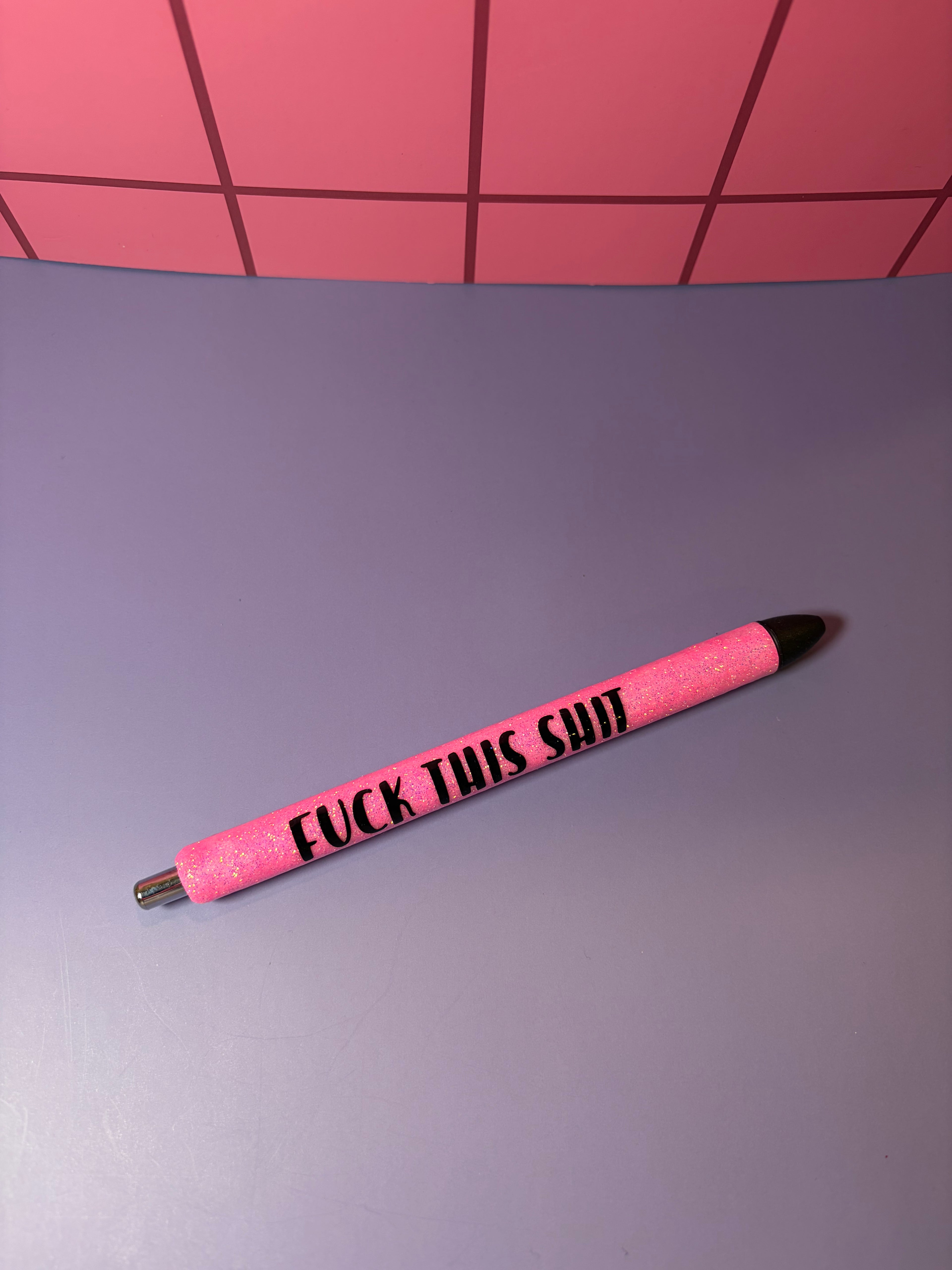Pink pen with black text on a gray surface with a pink grid background