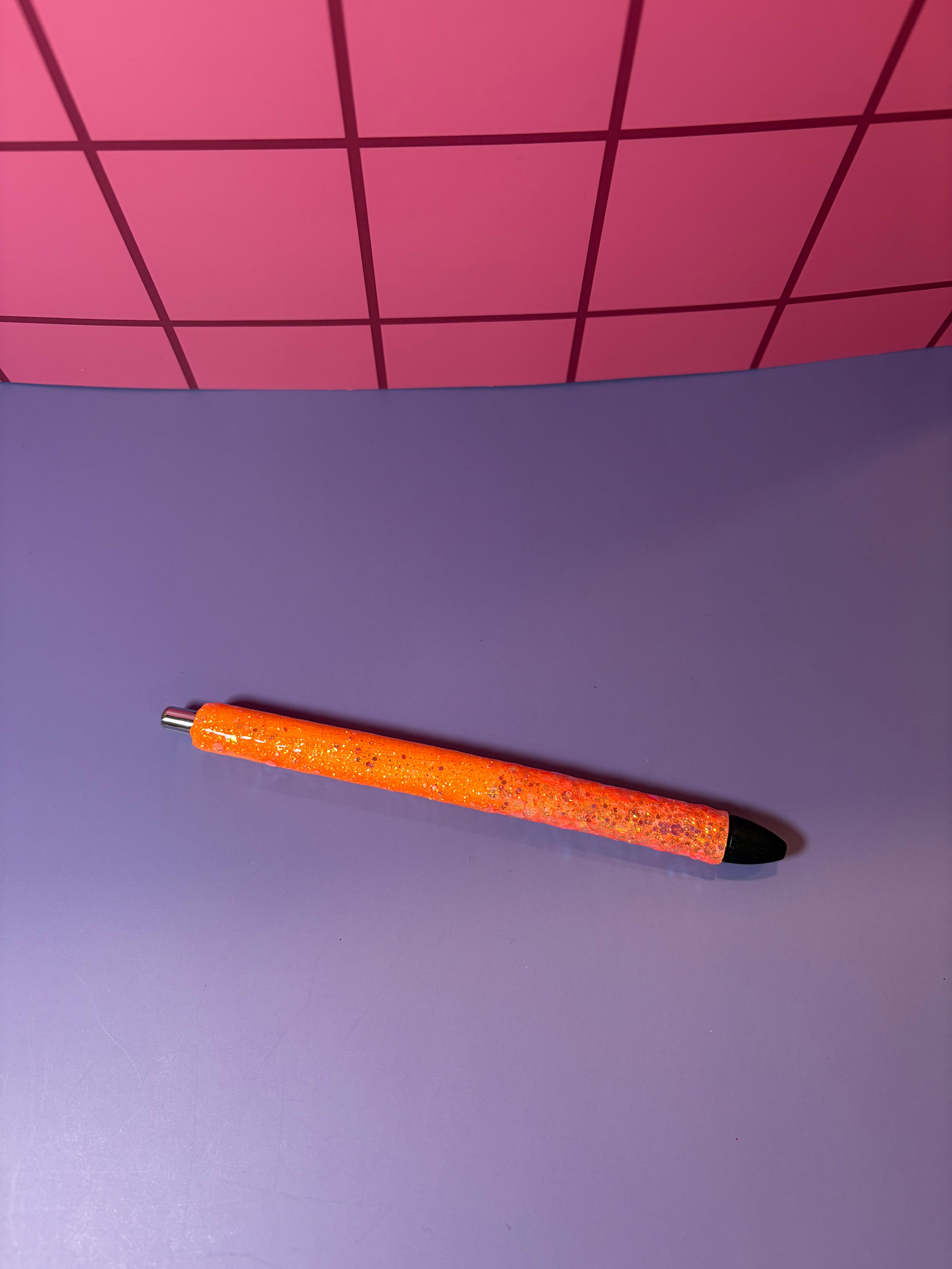 Orange pen with black cap on a purple surface with pink grid background