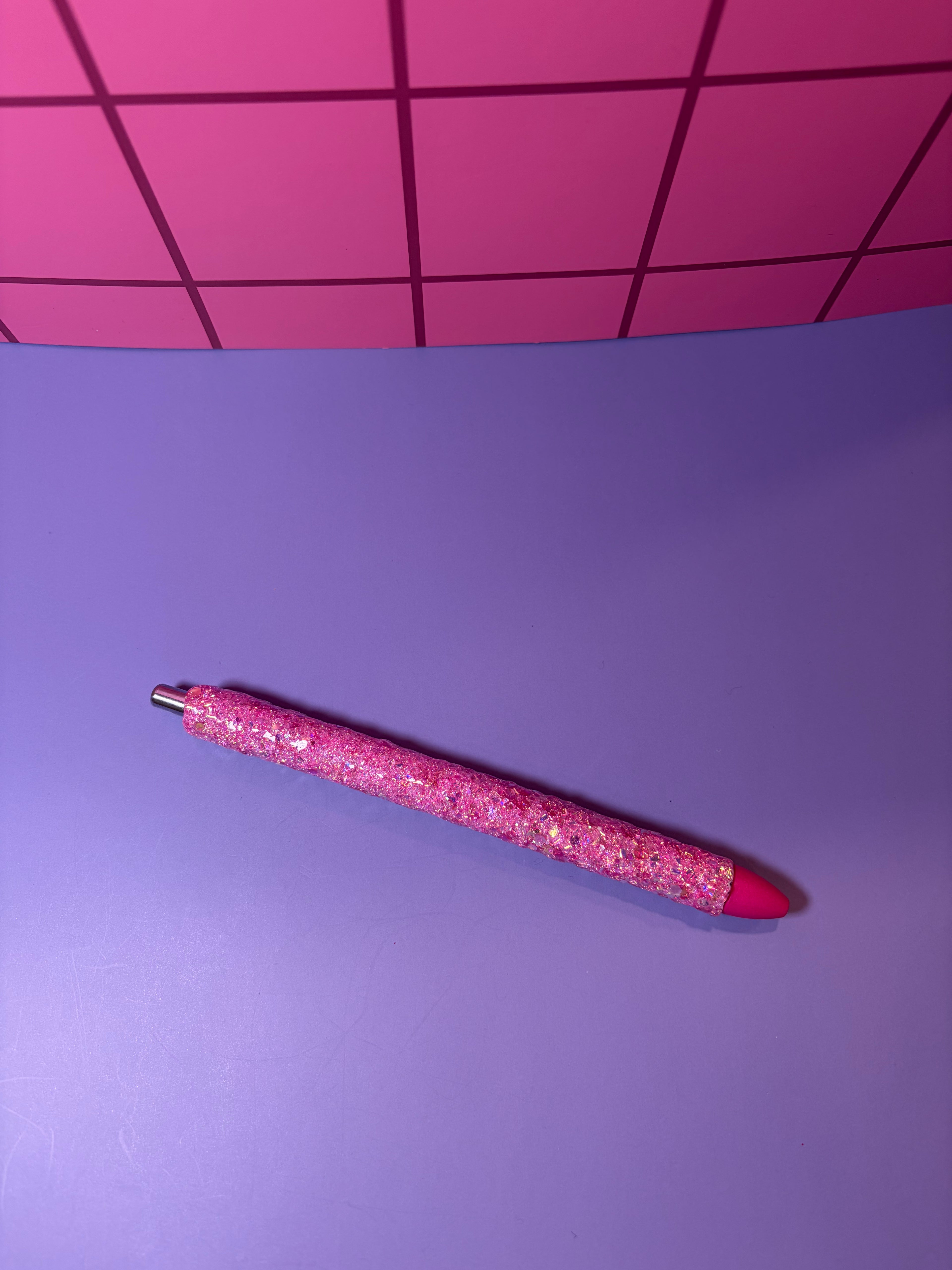 Pink glittery pen on a purple surface with a pink grid background