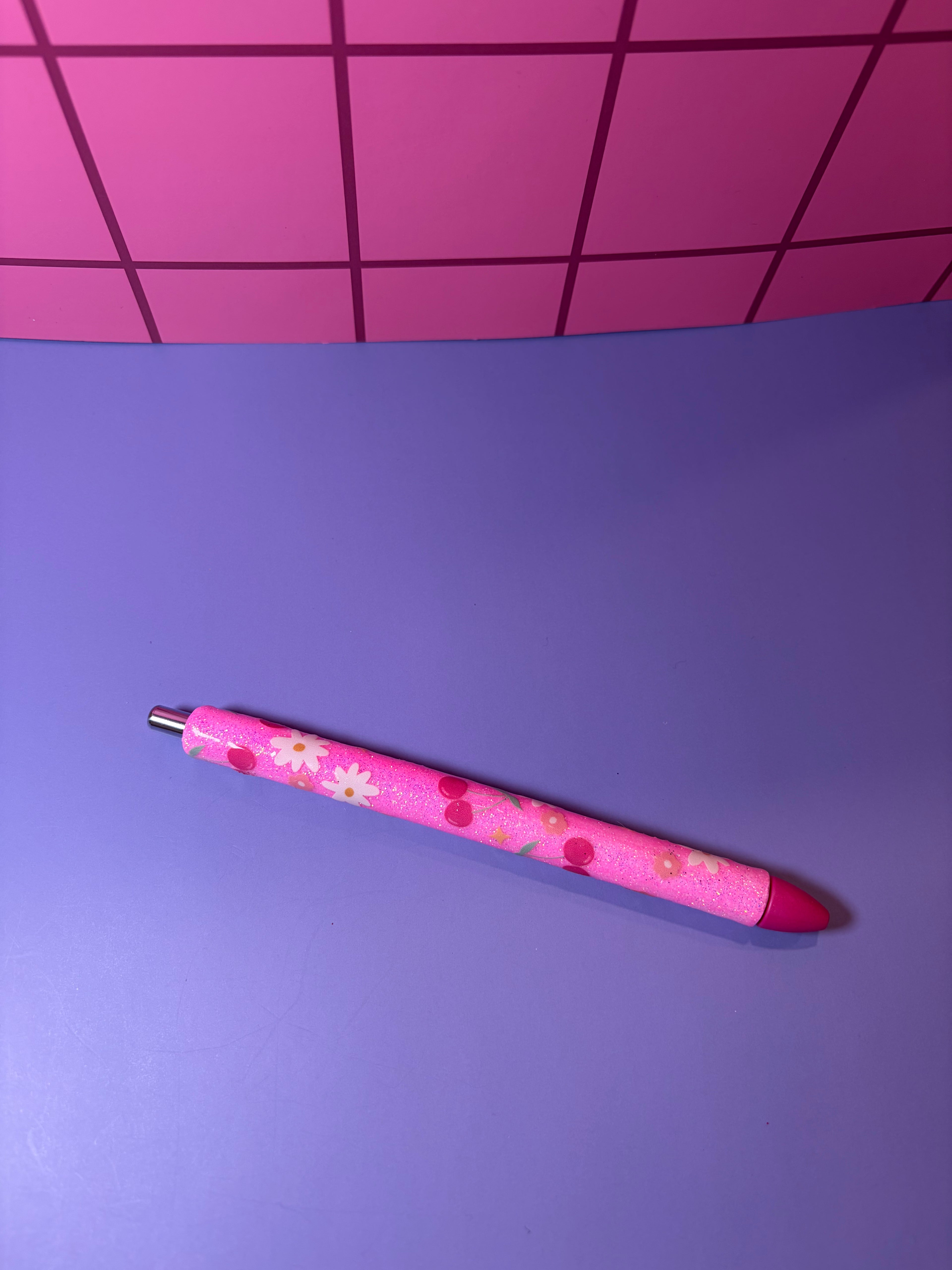 Pink pen with floral design on a purple surface with pink grid background