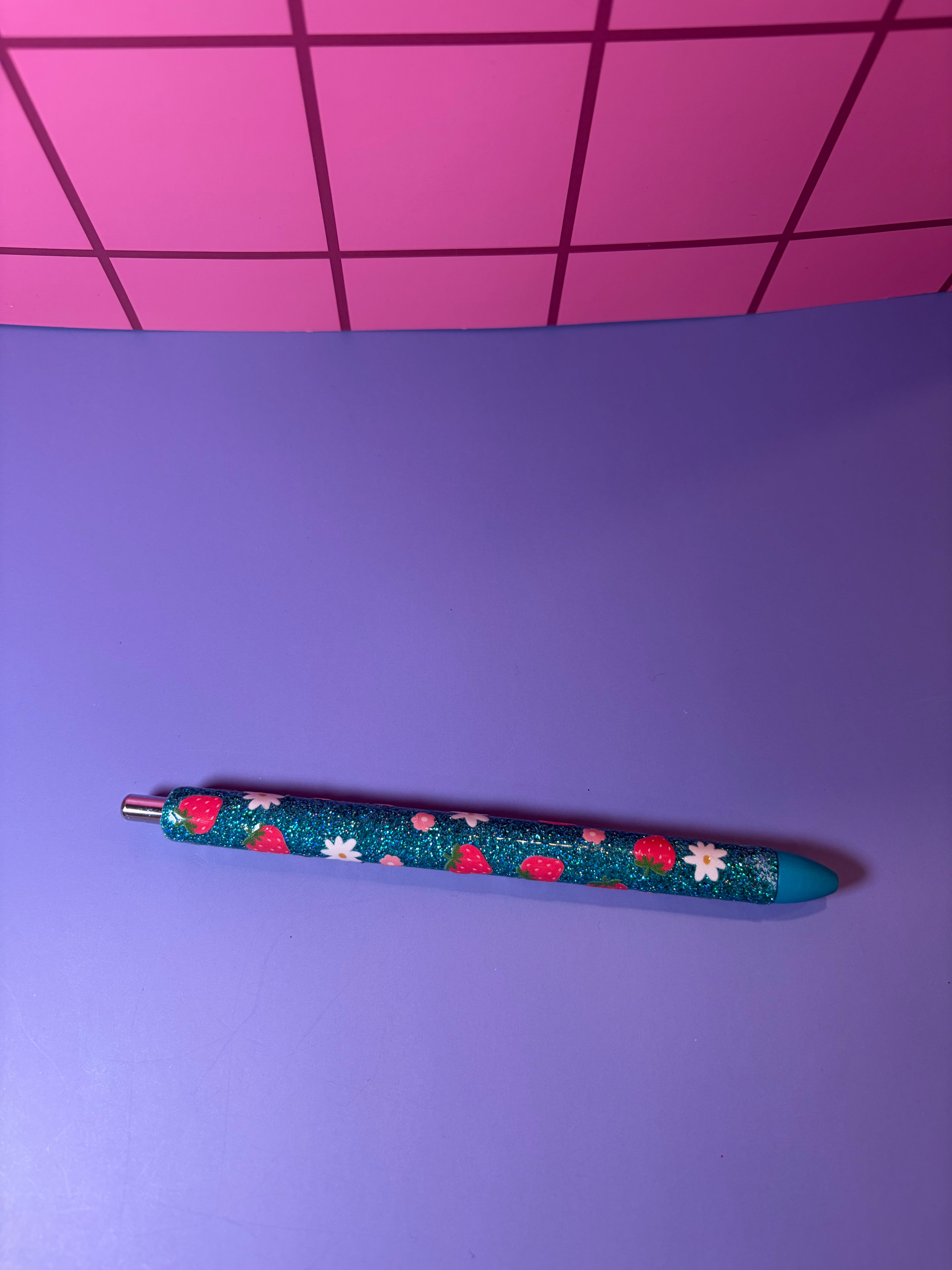 Decorative blue pen with floral pattern on a purple surface with pink grid background