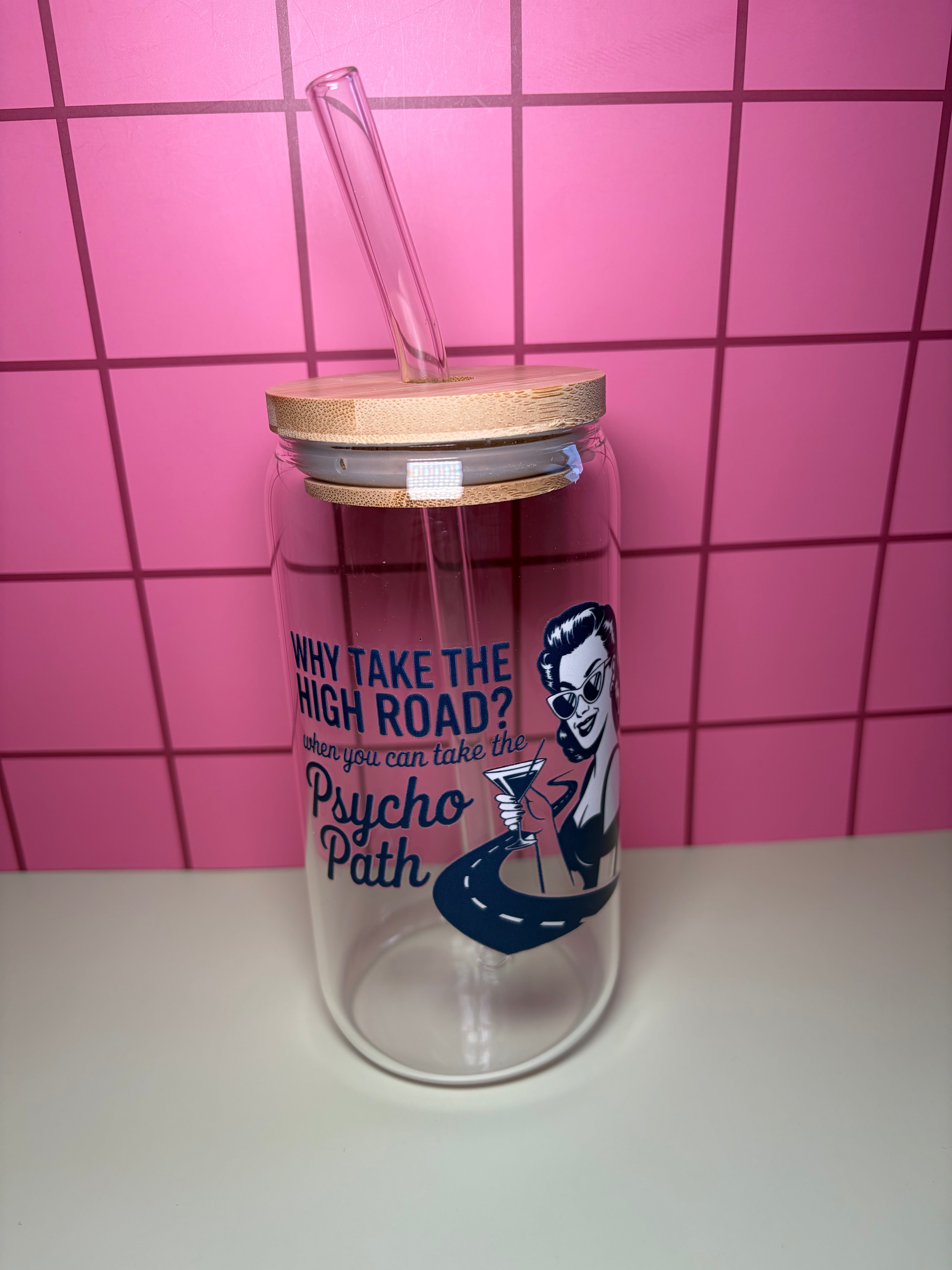 Glass can with wooden lid and straw. The decal on the can says why take the high road when you can take the psycho path with an image of a woman holding a cocktail. 
