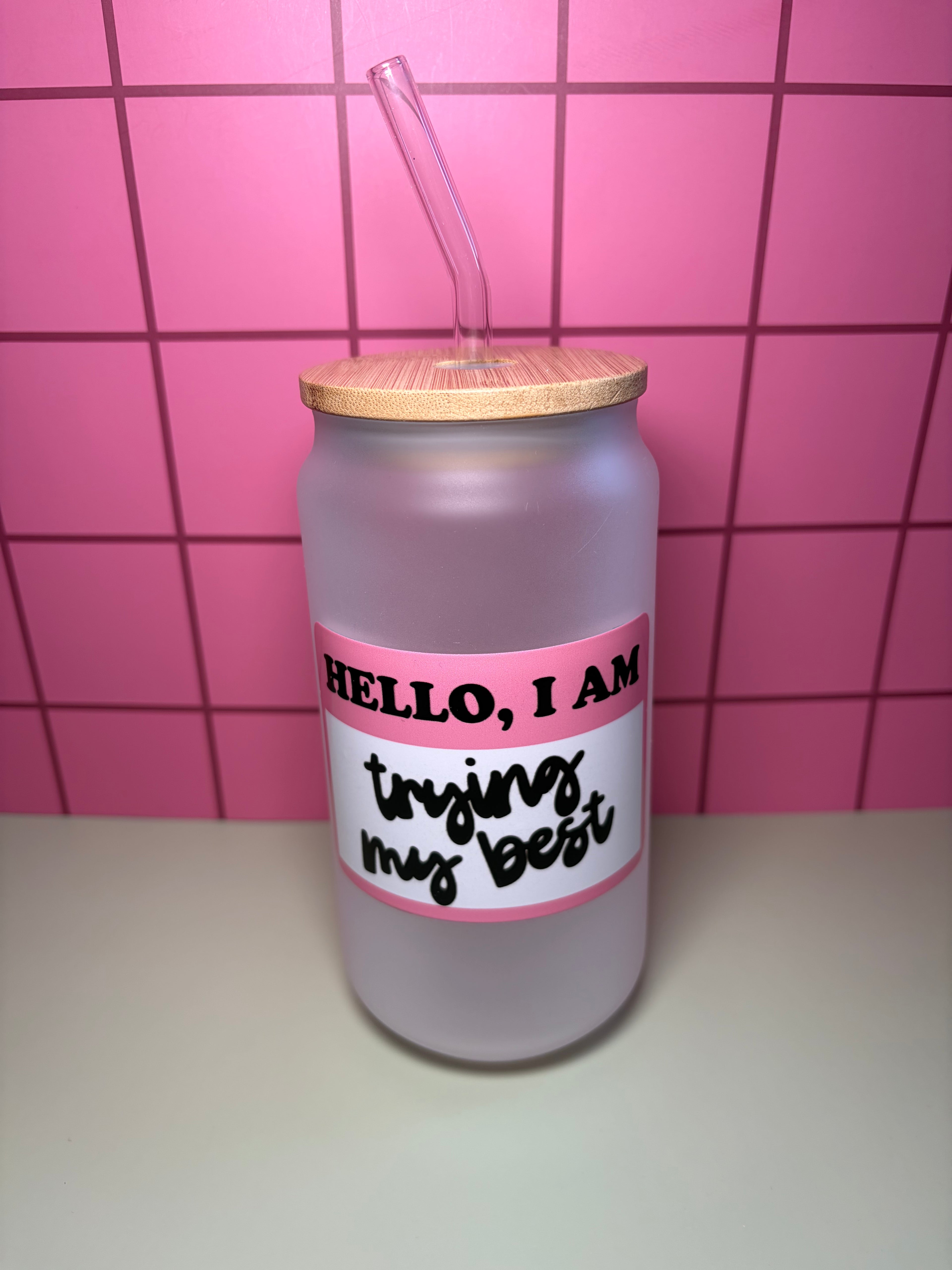 frosted glass cup with wooden lid and straw. the decal is a pink and says hello I am trying my best. 