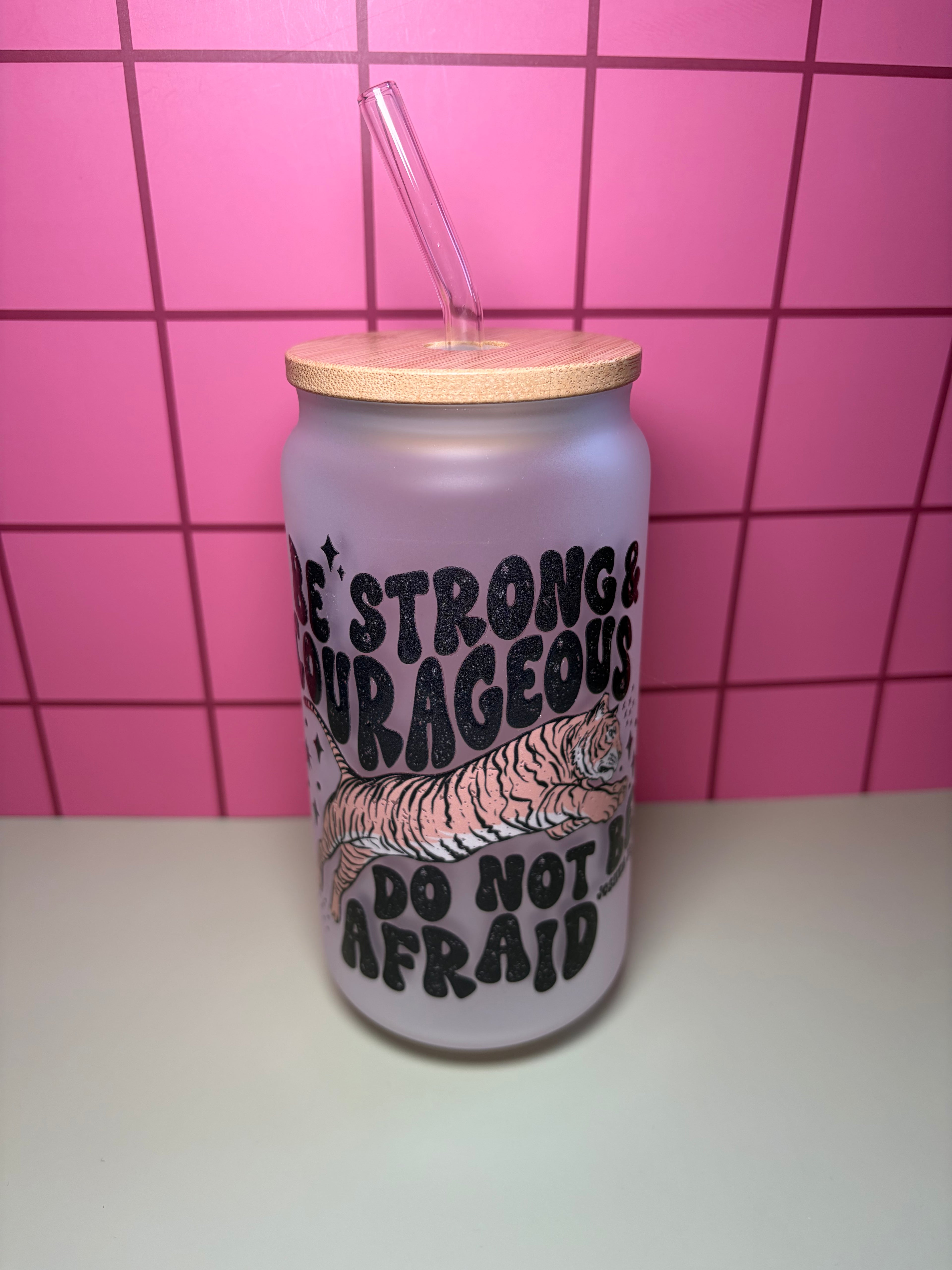 Frosted glass cup with wooden lid and straw. The decal is black text that says be strong & courageous and do not be afraid. There is a tiger on the decal. 