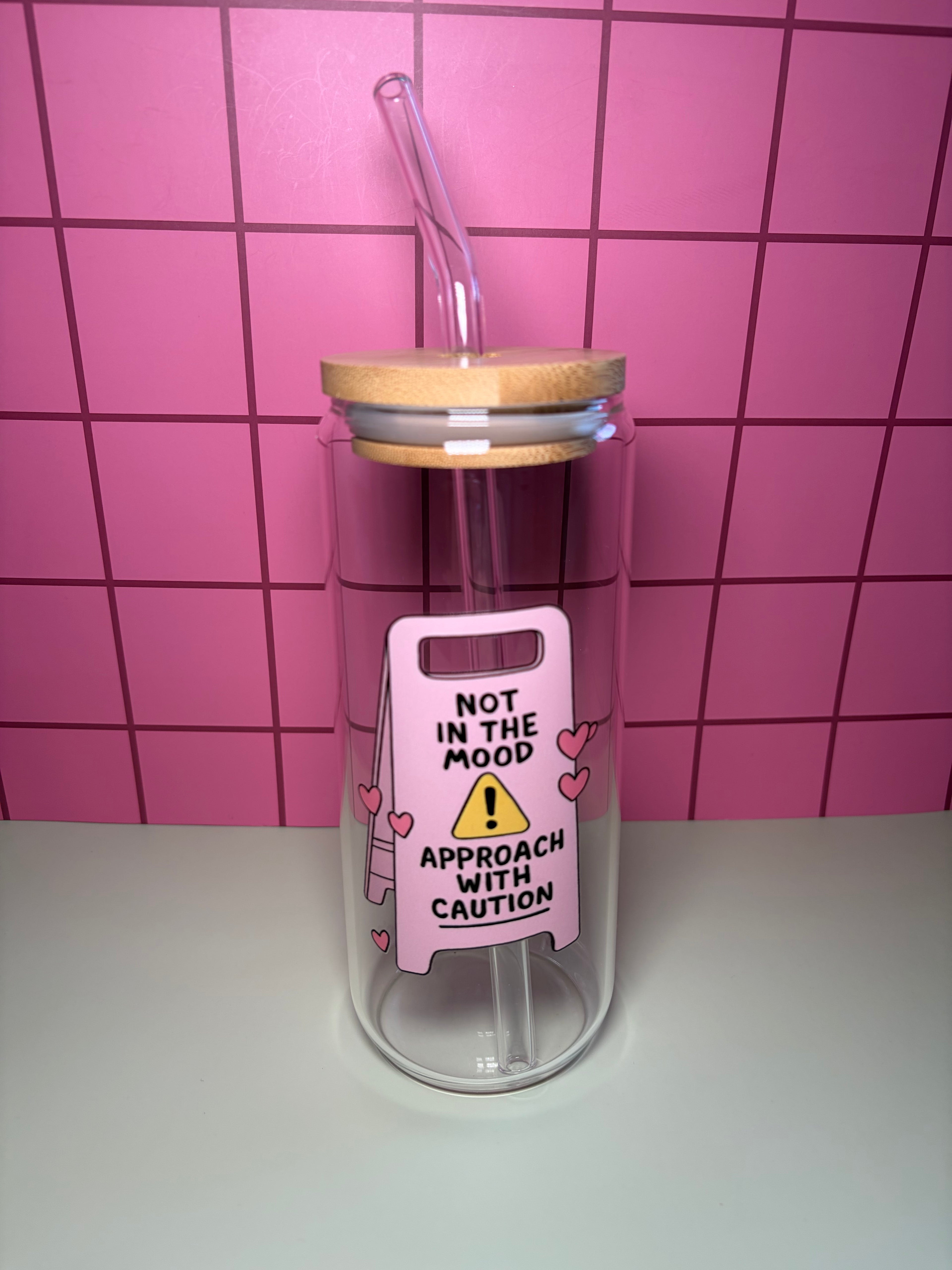 20 oz glass can with wooden lid and straw. The decal is a pink sign that says not in the mood approach with caution. 