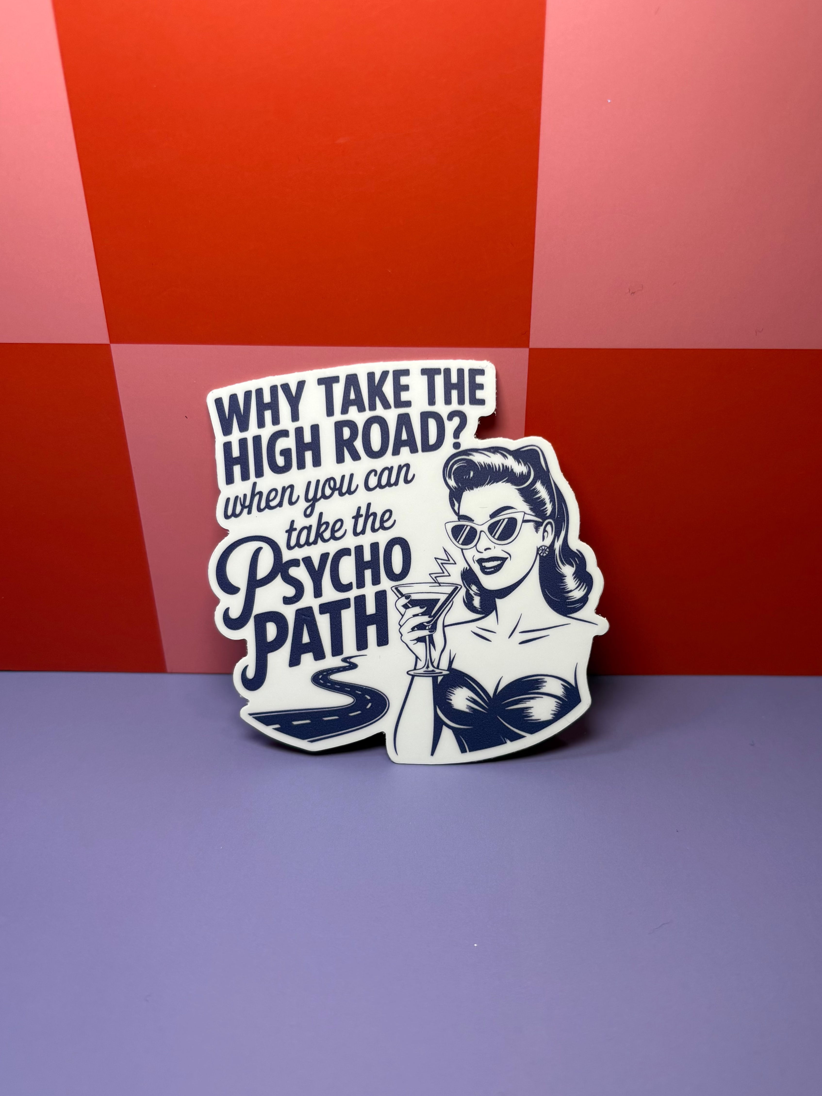 Sticker with "Why Take the High Road? When you can take the psycho path" text and graphic design on a red and purple checkered background