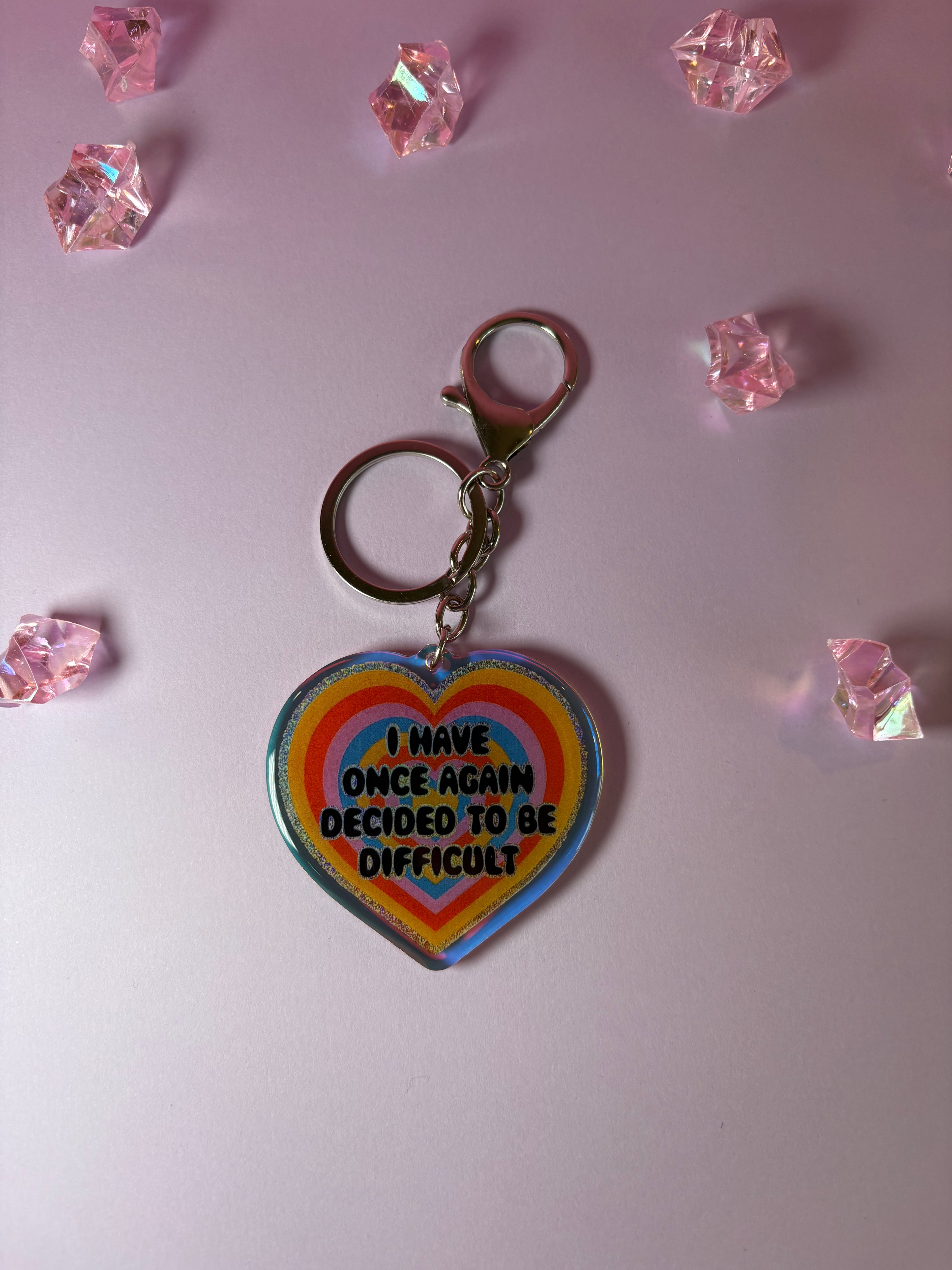 Heart-shaped keychain with rainbow border and text "I have one again decided to be difficult"