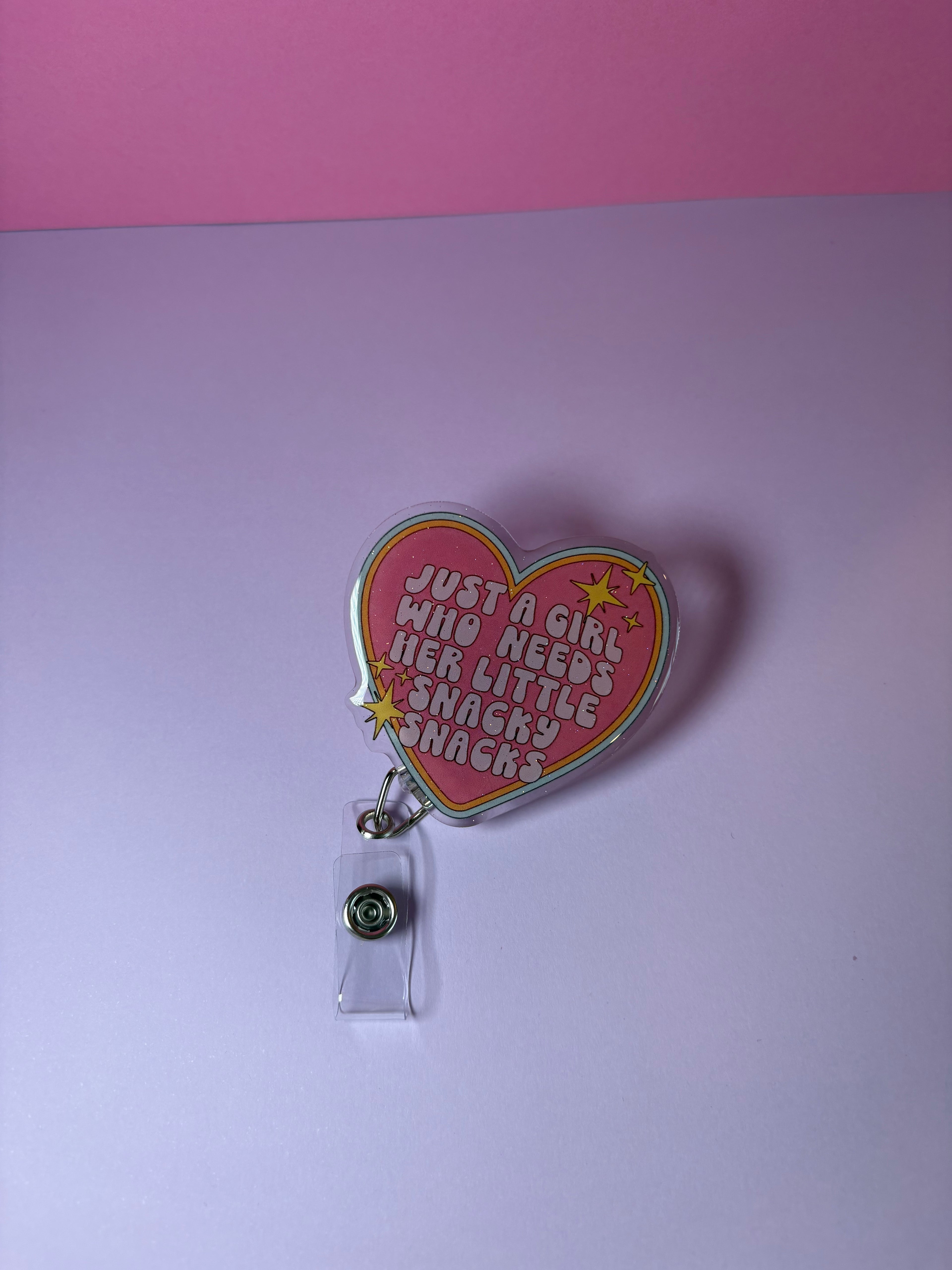 Heart-shaped badge holder with text "just a girl who needs her little snacky snacks"