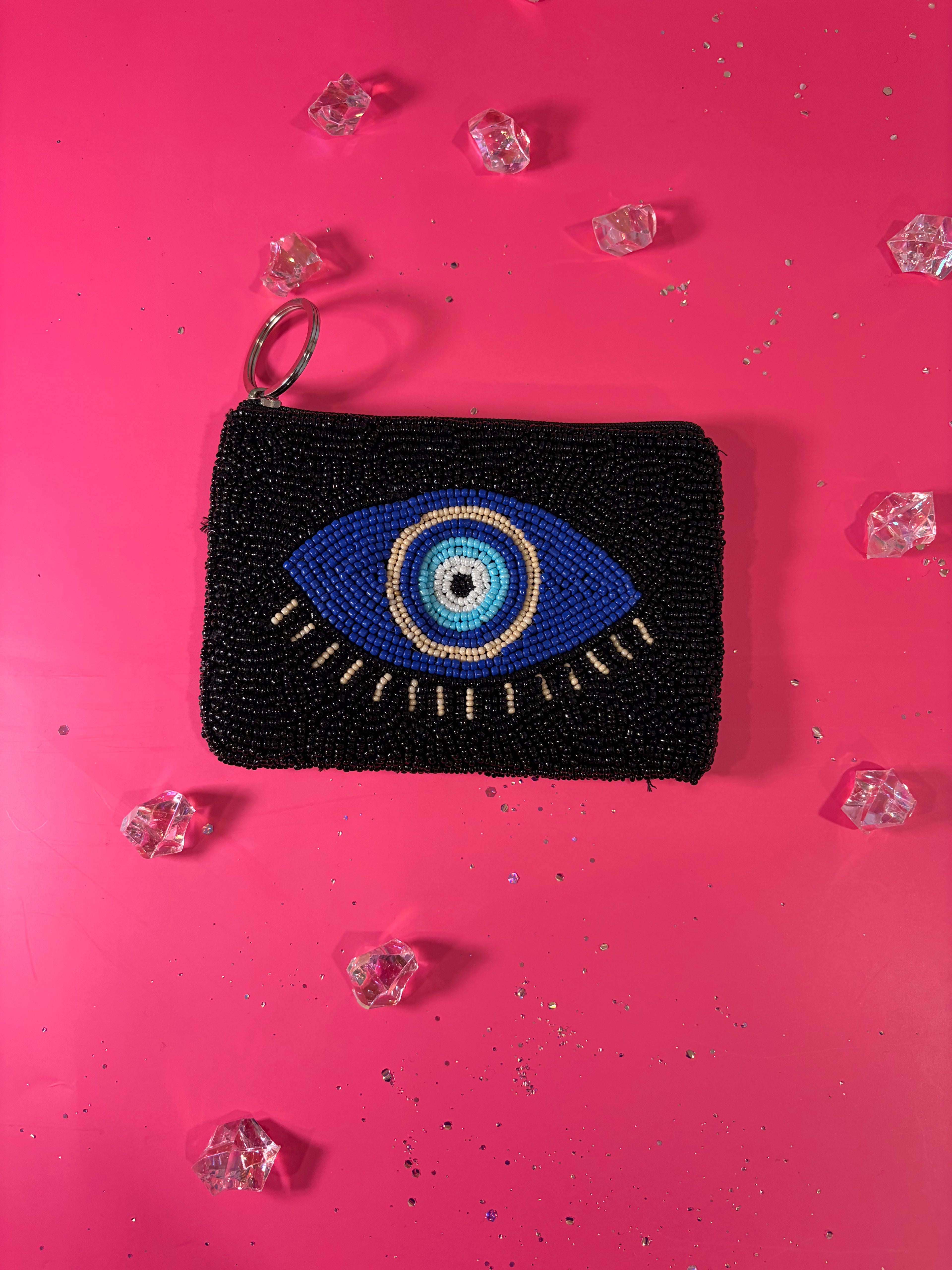 Black beaded pouch with eye design on a pink background with decorative crystals.
