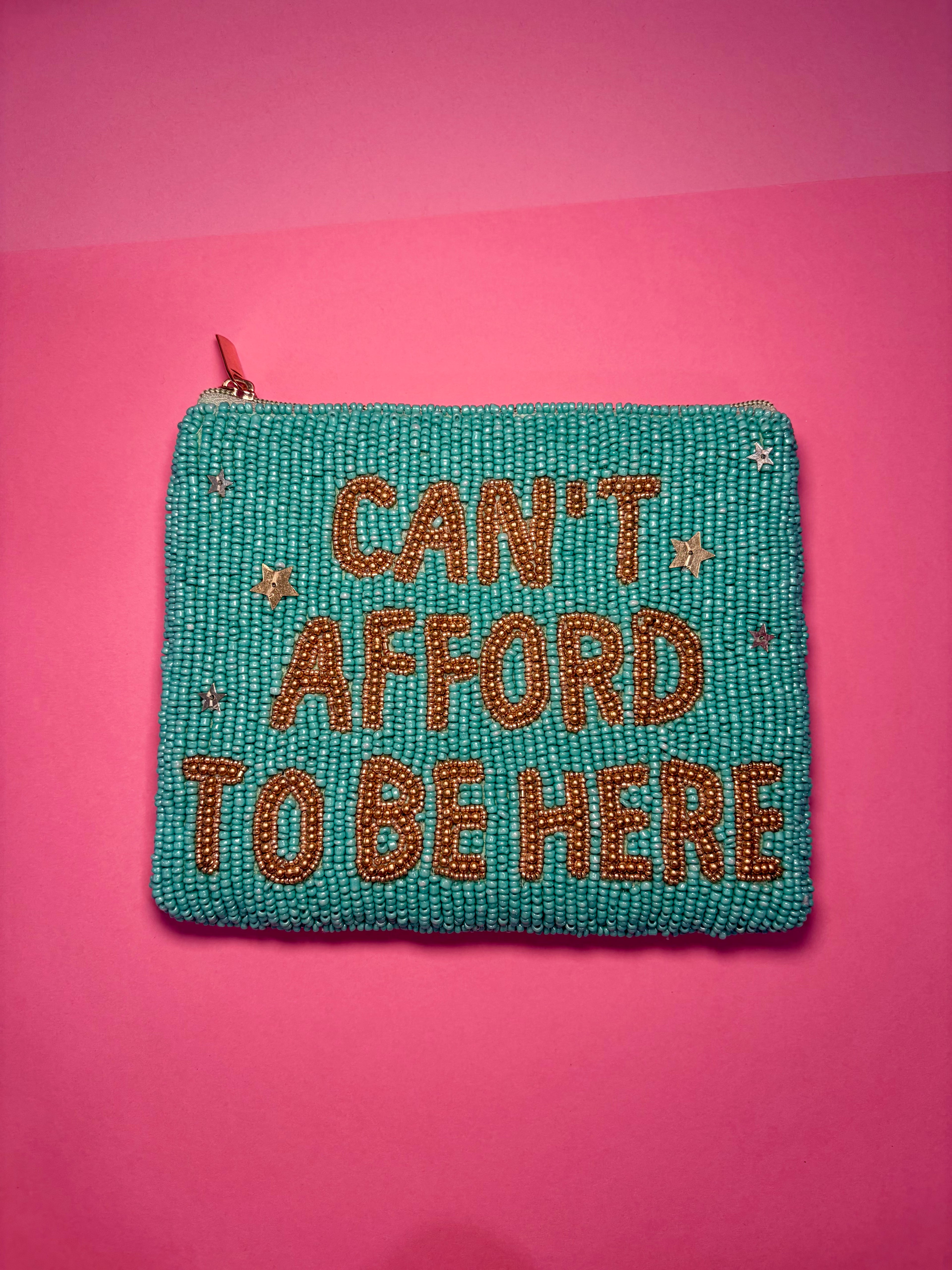 Teal beaded pouch with 'Can't Afford To Be Here' text on a pink background