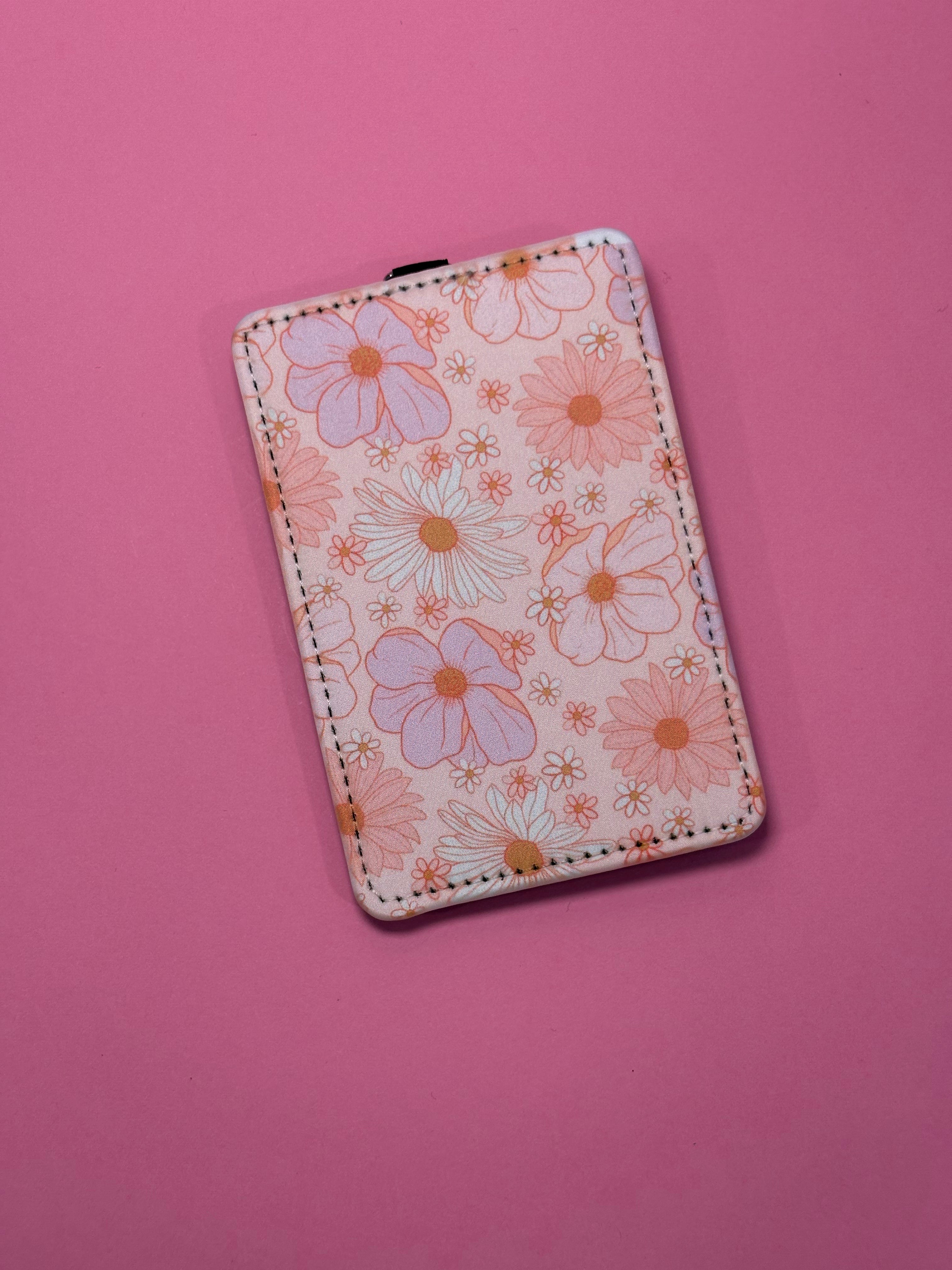 A rectangular ID badge holder a pink and orange floral pattern, shown on a solid pink background.