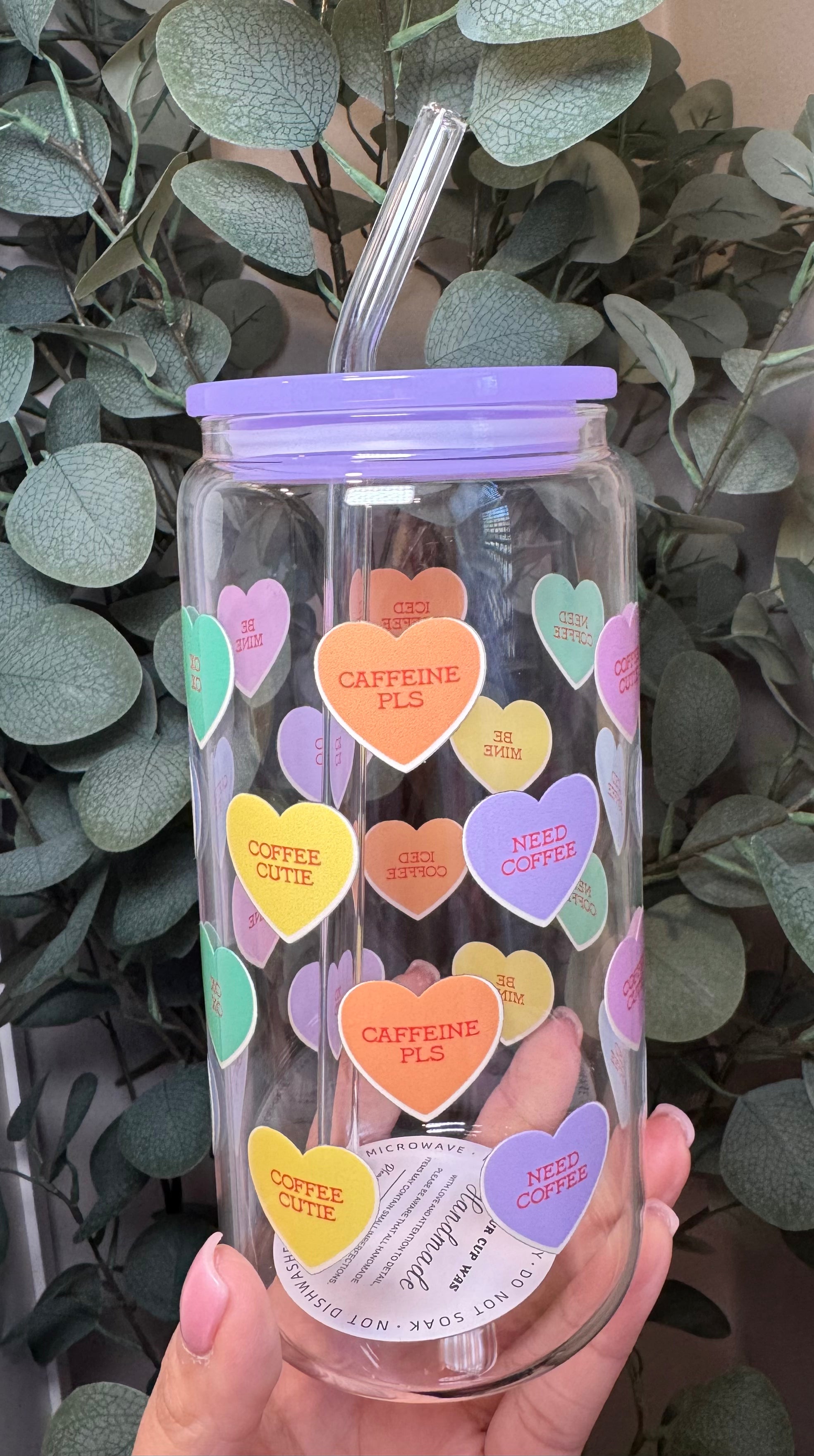 Clear tumbler with purple lid colorful heart-shaped stickers held in front of green leaves