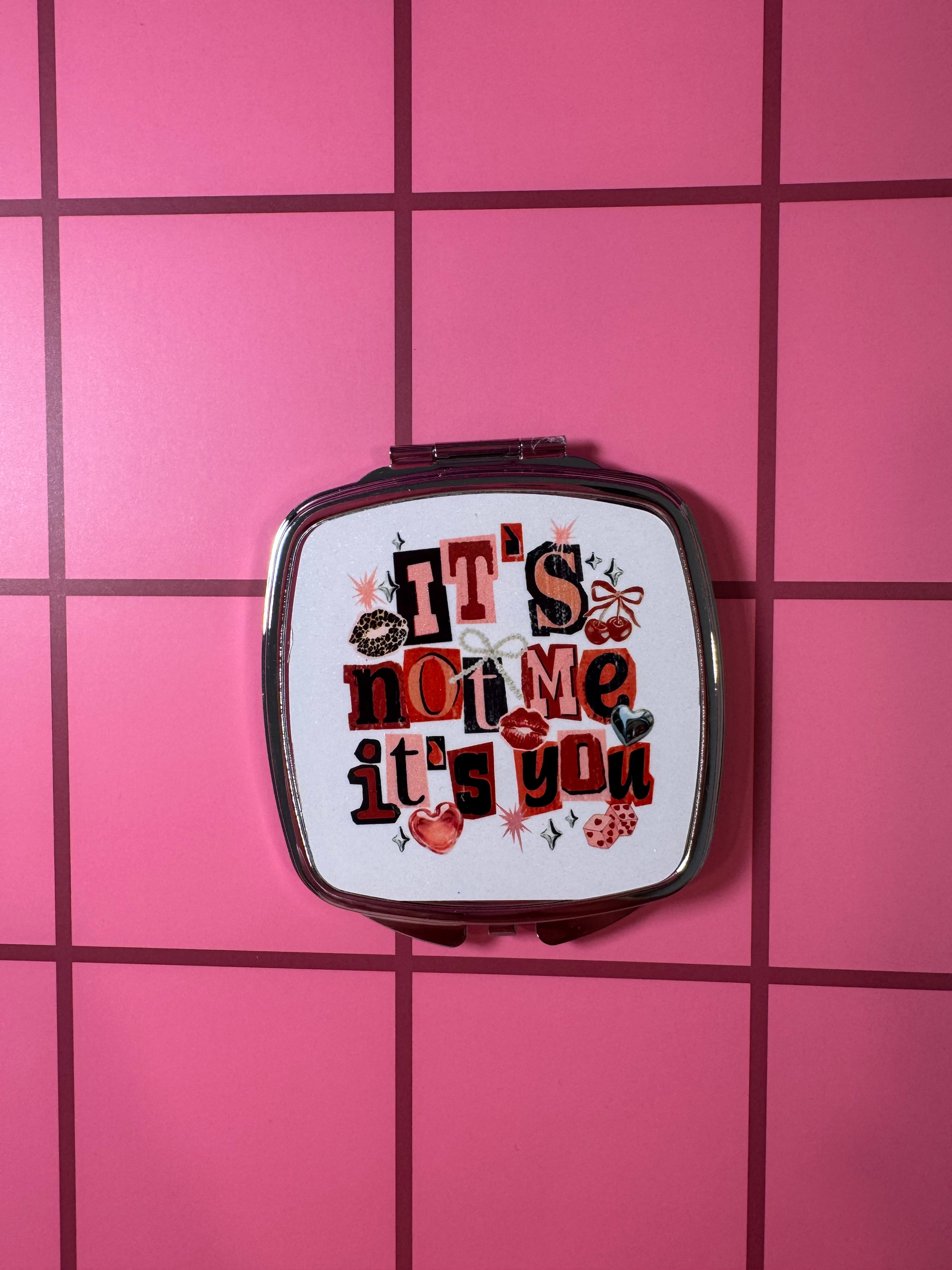 Compact mirror with 'It's not me, it's you' colorful pink text on a white background