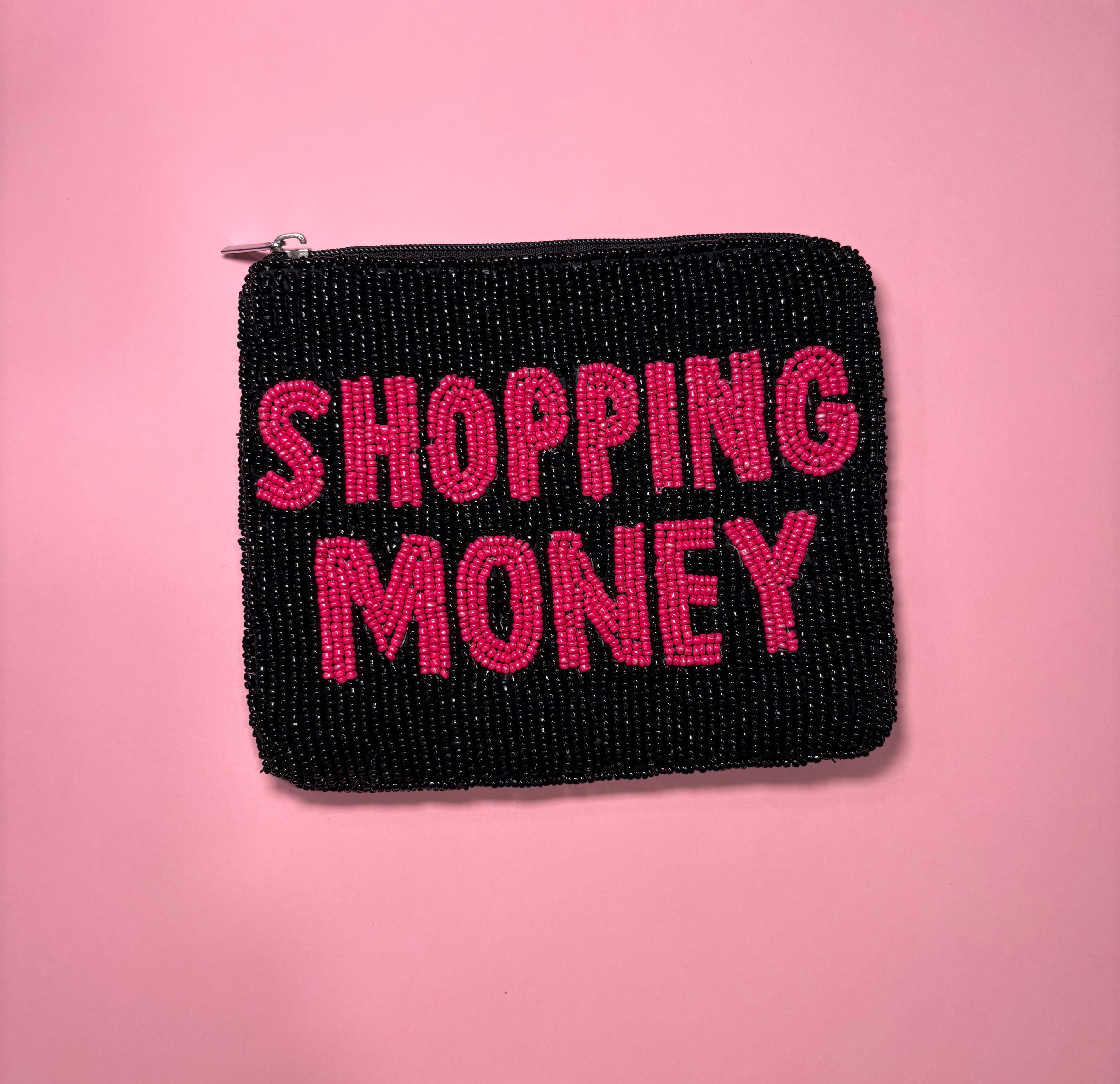 A black beaded zippered pouch with the words 'SHOPPING MONEY' in bright pink beaded letters, set against a solid pink background.